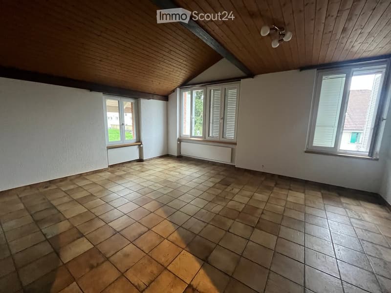 Empty room with wooden slanted ceiling, tiled floor, and multiple windows with shutters. No furniture or equipment present.