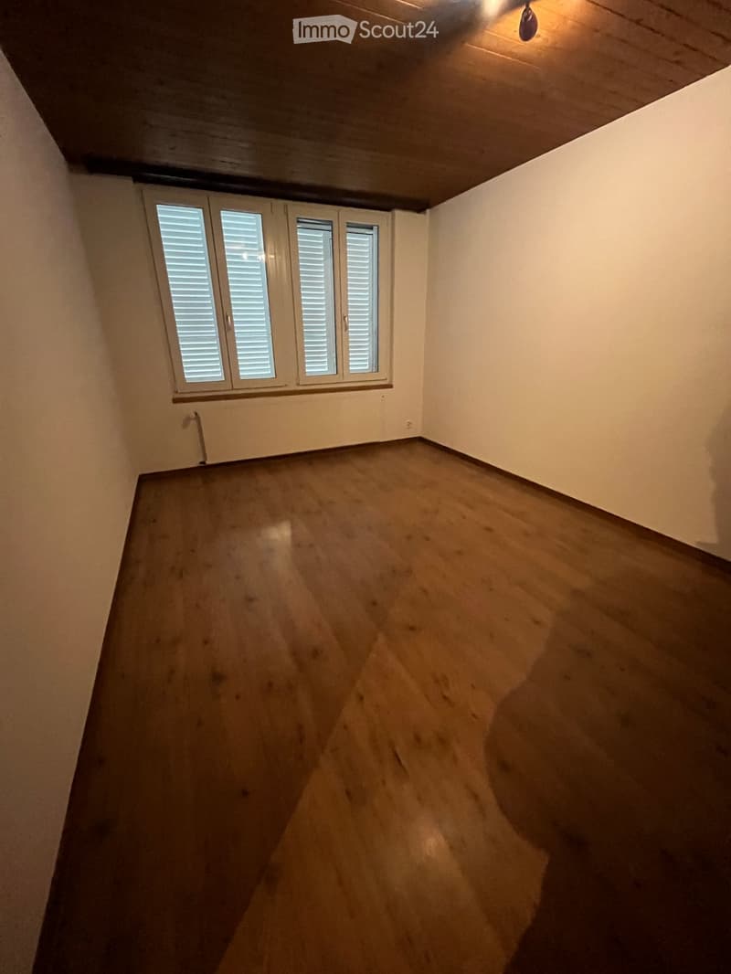 Empty room with wooden floor and white walls, featuring a window with white shutters and a ceiling light fixture.