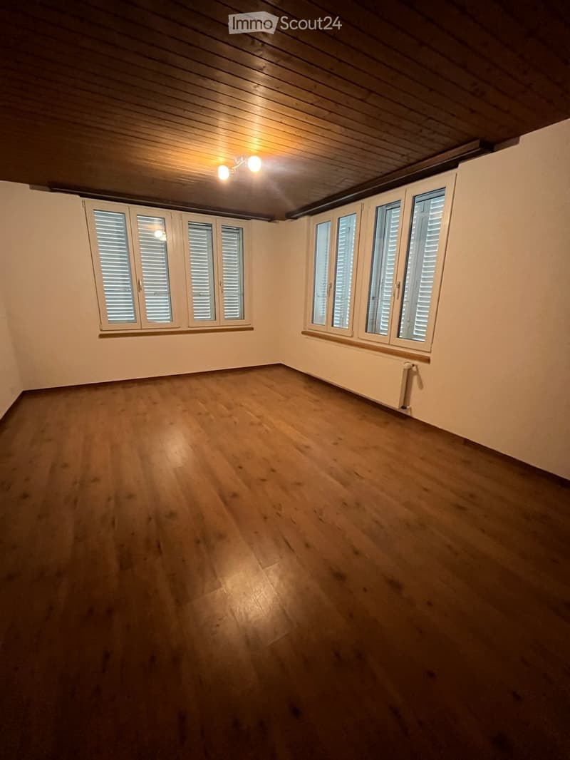 Empty room with wooden flooring, white walls, and multiple windows with blinds. The ceiling has exposed wooden beams and recessed lighting.