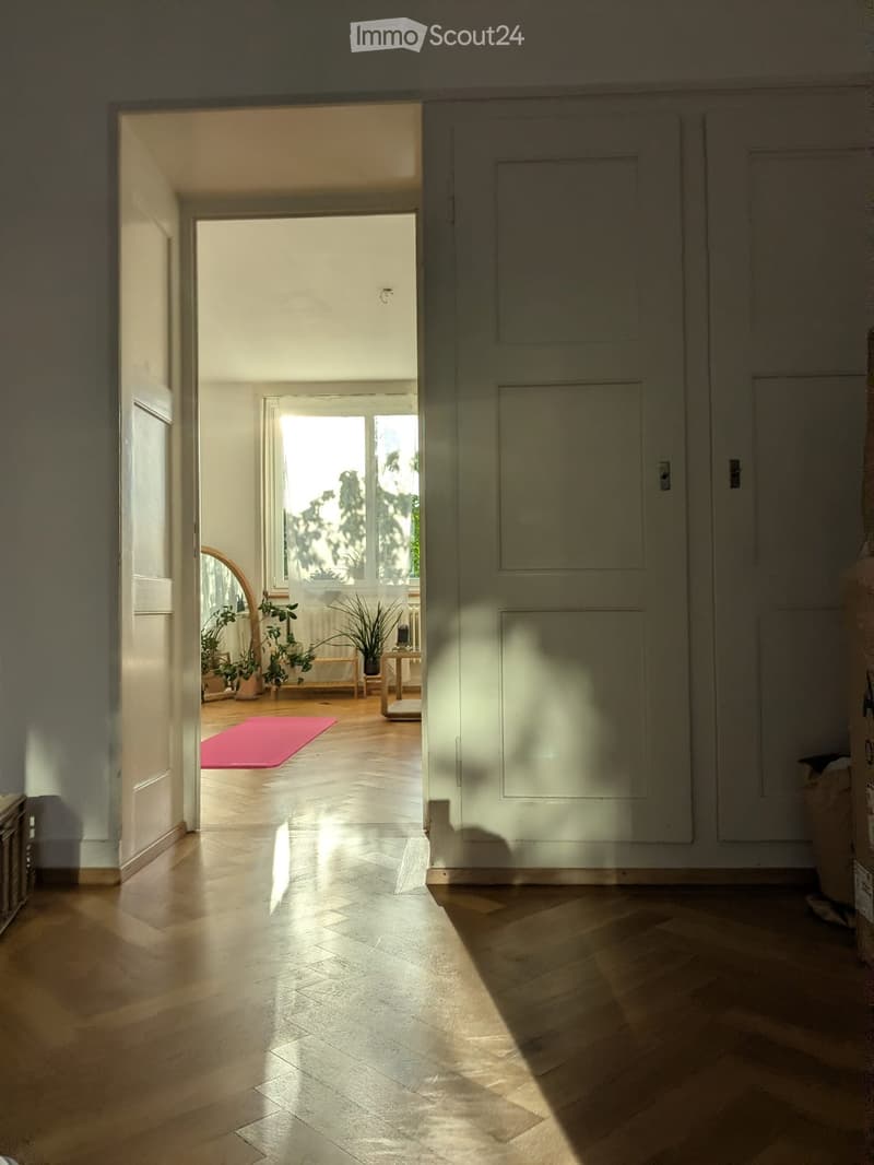 Bright hallway with wooden flooring, leading to a room with plants and a pink mat.