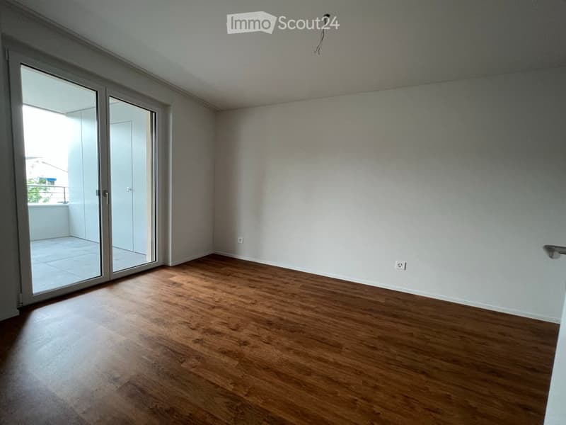 Empty room with wooden flooring, white walls, and large sliding glass doors leading to a balcony.