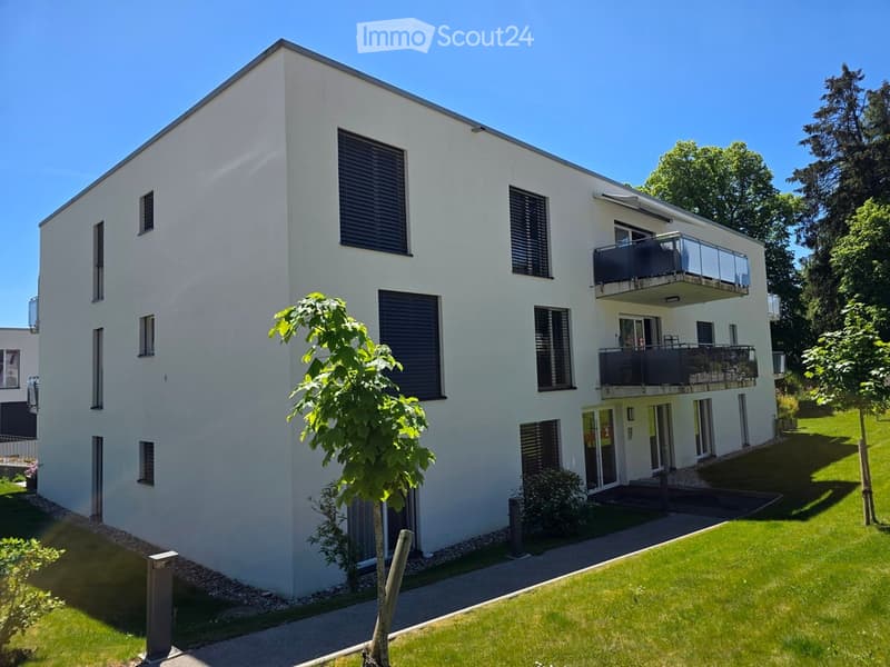 Modern two-story white building with multiple windows, balconies, and a small garden area.
