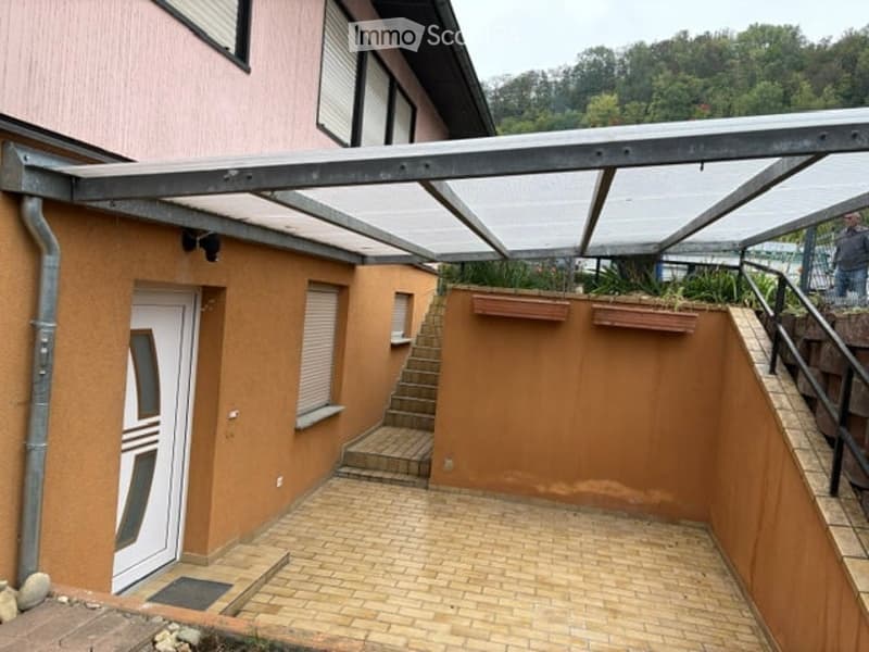 Brick patio area with a covered walkway, steps leading up to a raised section, and planters on the wall.