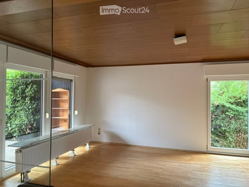 Empty room with wooden flooring, white walls, large windows, and a radiator under one window.