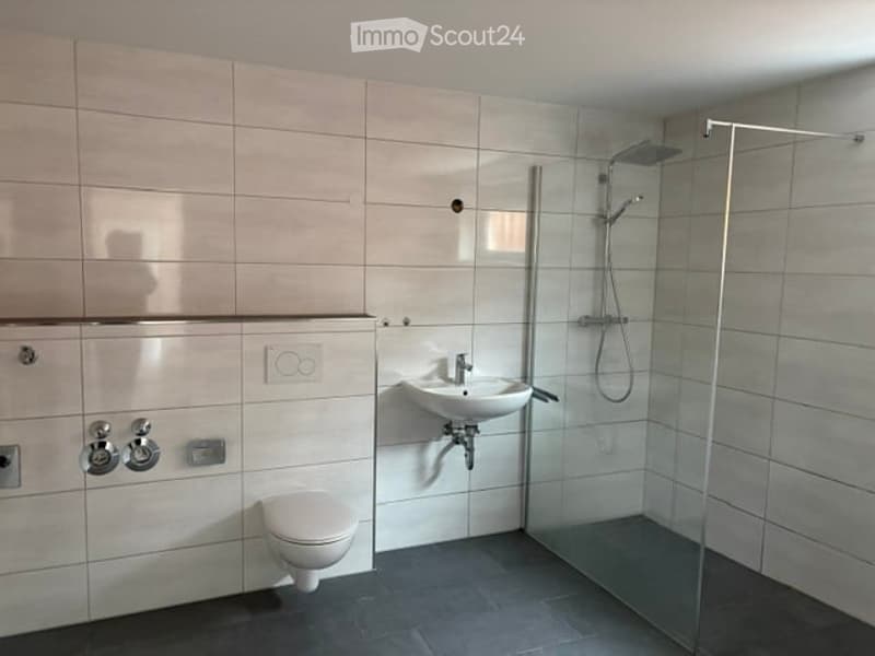 Modern bathroom with white tiles, a toilet, a sink with a faucet, and a glass-enclosed shower area.