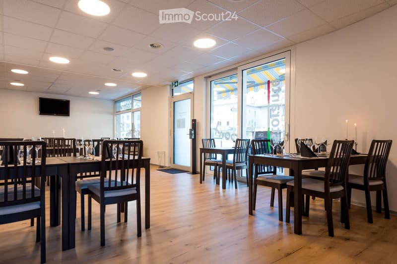 Restaurant or dining area with wooden tables, chairs, wine glasses, and a television mounted on the wall.