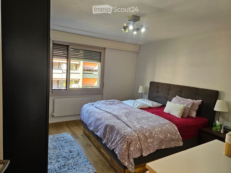 Cozy bedroom with a large bed, patterned duvet, nightstands, lamps, and a rug on the wooden floor.