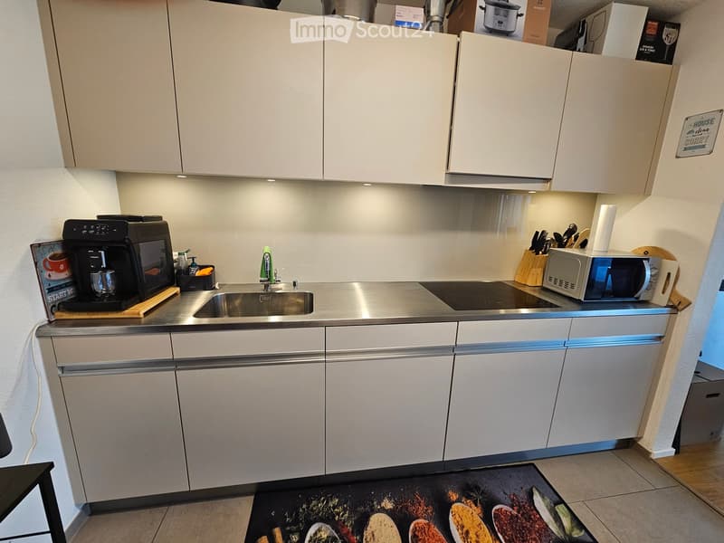 Modern kitchen with white cabinets, stainless steel sink, induction cooktop, microwave, coffee maker, and knife block.