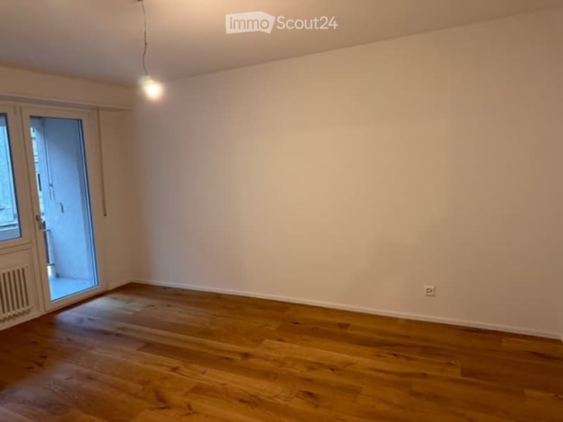 Empty room with wooden flooring, white walls, and a large glass door leading to a balcony.