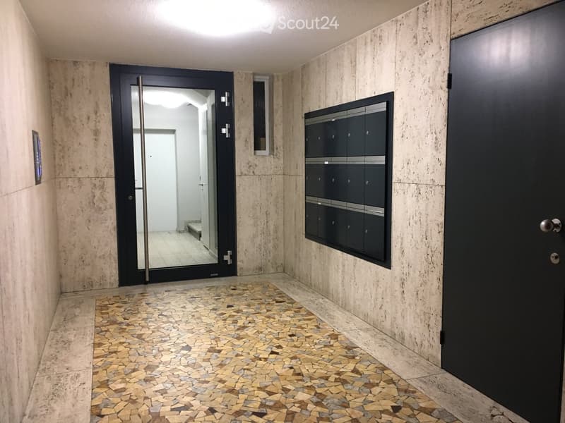 Modern hallway with beige marble walls, mosaic tile floor, black mailboxes, and a glass door leading to another area.