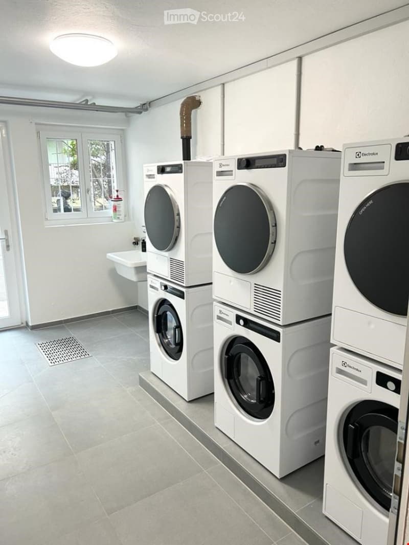 Clean, modern bathroom with tiled floor, white walls, and multiple stacked washing machines and dryers.