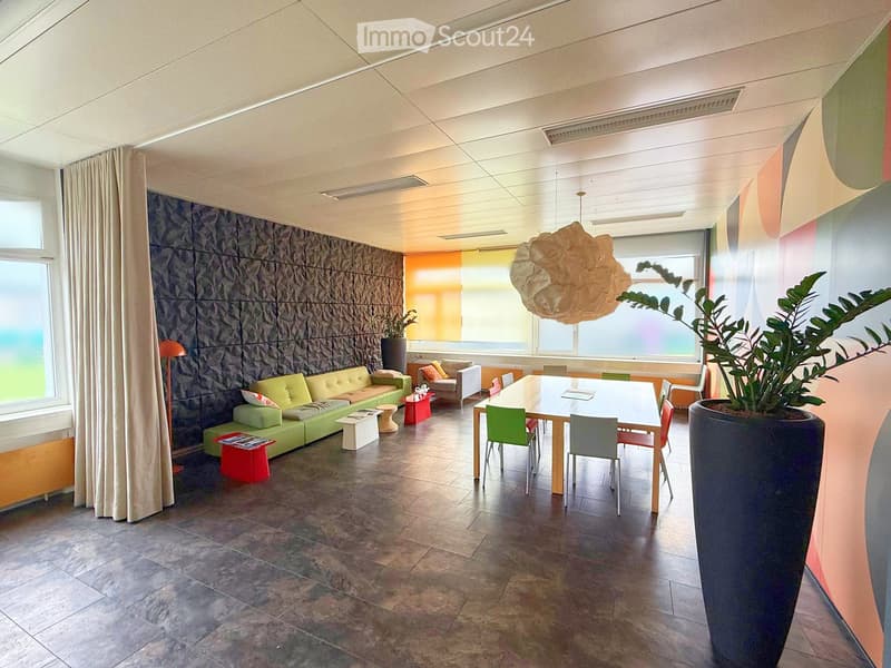 Modern living room with a green sofa, dining table, chairs, decorative stools, a large plant, and a hanging light fixture.