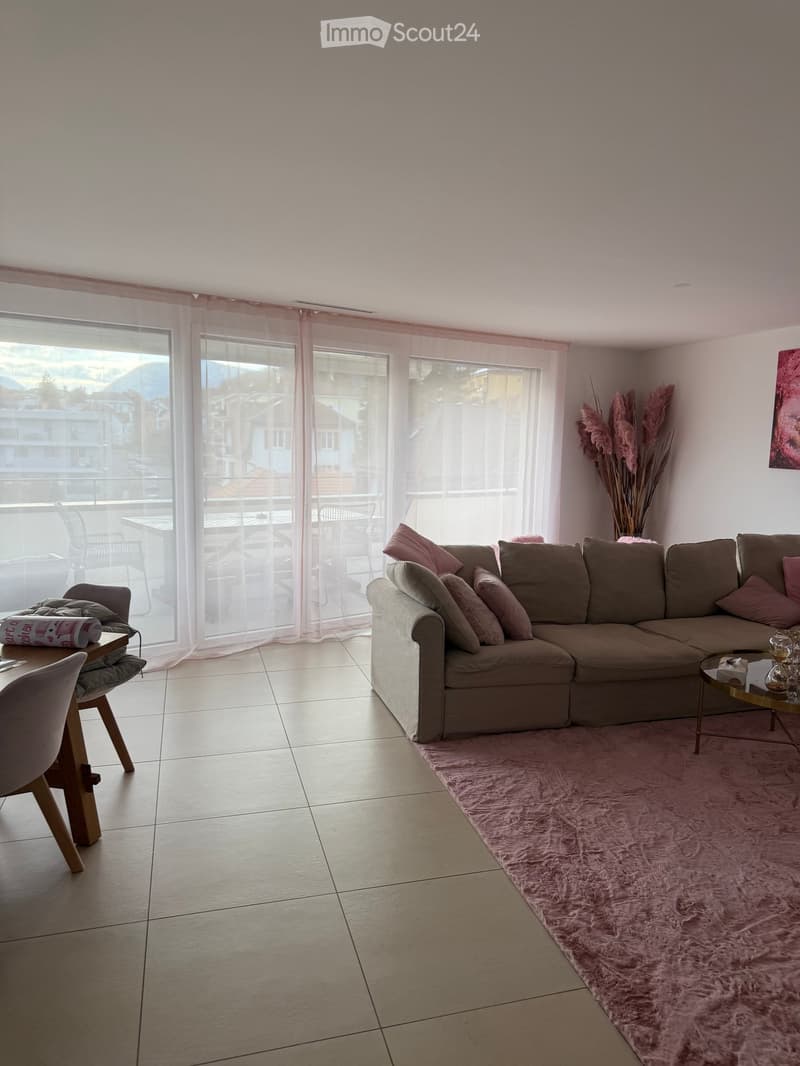 Modern living room with a large sectional sofa, pink throw pillows, a round coffee table, a pink shag rug, and a view of the balcony area.