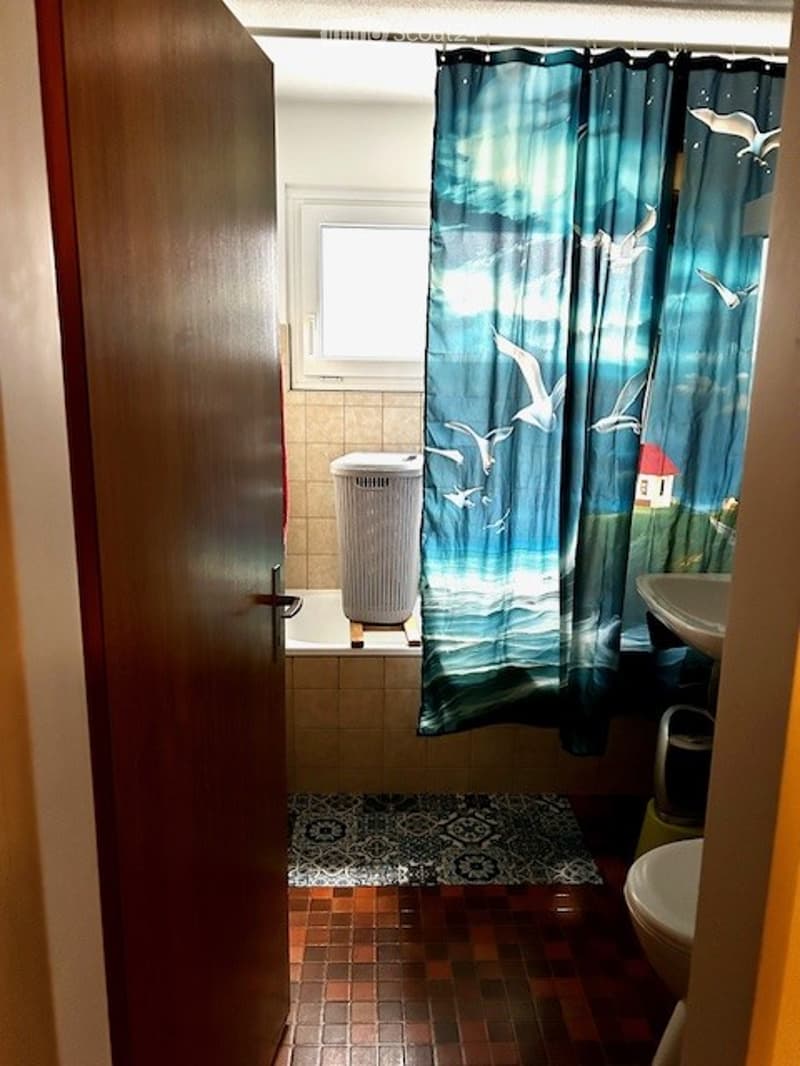 Bathroom with a bathtub, toilet, sink, and a blue curtain with a bird and house design. The floor has a patterned tile design.
