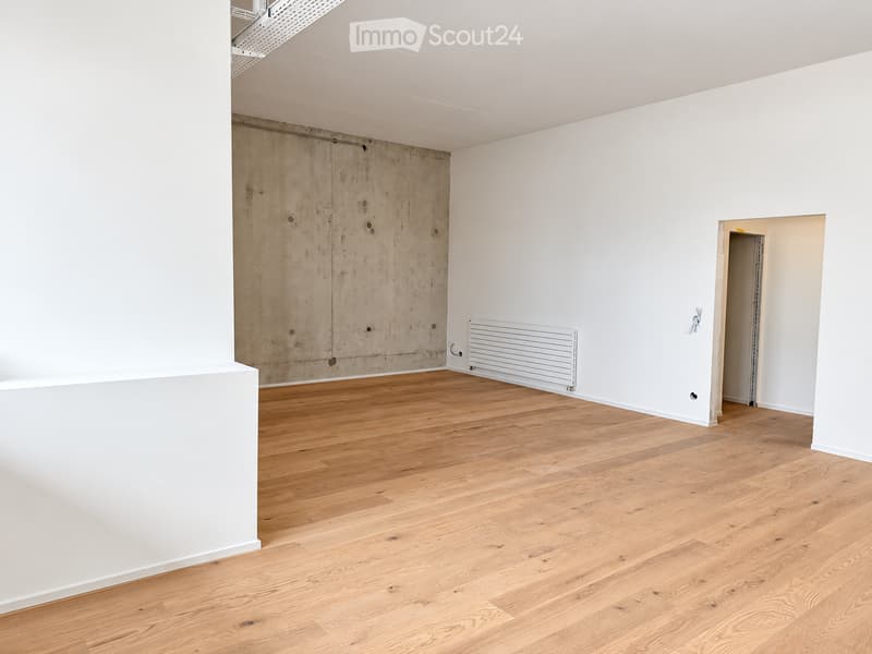Empty room with light wooden flooring, white walls, and a radiator on one wall. A doorway leads to another space.