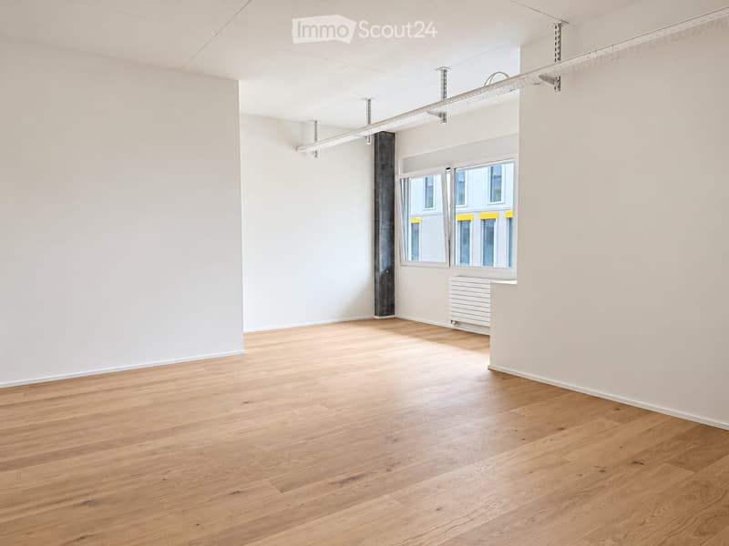 Empty room with light wooden flooring, white walls, and large windows with yellow frames. No furniture or equipment present.