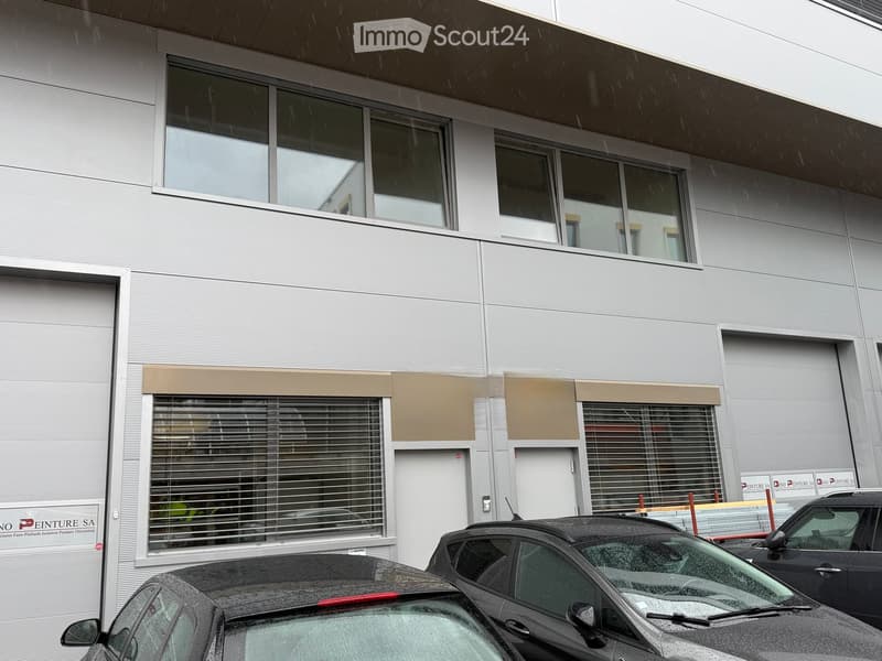 Modern two-story building with large windows, closed blinds, and a sign for "Peinture SA" on the ground floor. Two cars are parked in front.