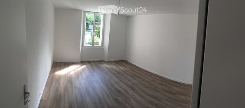 Empty room with wooden flooring and white walls, featuring a window with a view of greenery outside.