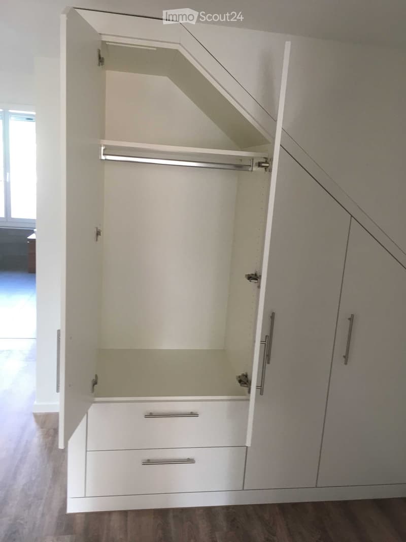 Empty room with white built-in closet featuring multiple shelves and drawers, wooden flooring, and a window in the background.