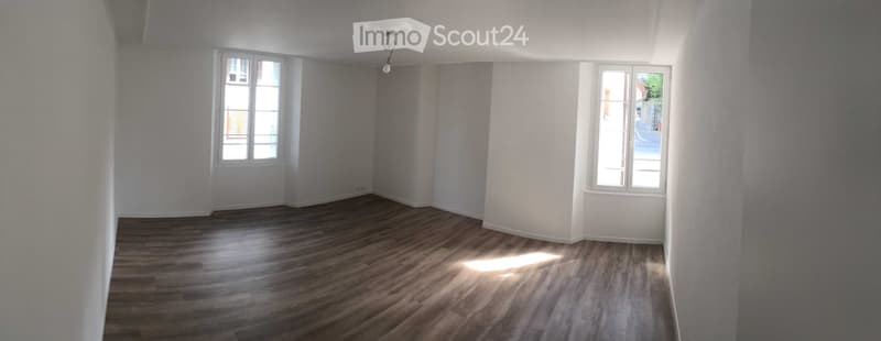 Empty room with wooden flooring, white walls, and two windows allowing natural light to enter.