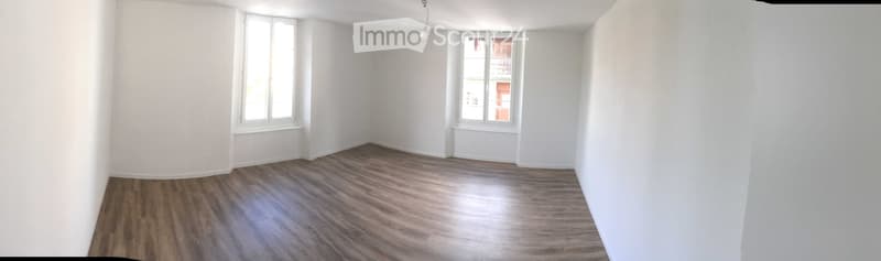 Empty room with wooden flooring and white walls, featuring two windows with white frames and a single ceiling light fixture.