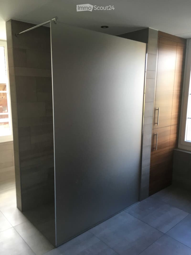 Empty bathroom with tiled floor, glass shower enclosure, and wooden cabinet.