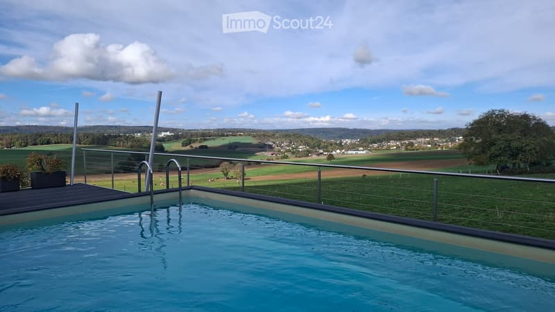Swimming pool with a modern metal railing, overlooking a rural landscape with fields and scattered houses.