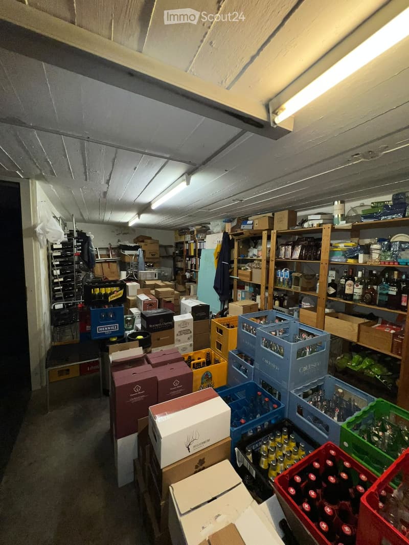 A cluttered storage room with shelves, boxes, crates, and various bottles stacked throughout the space.