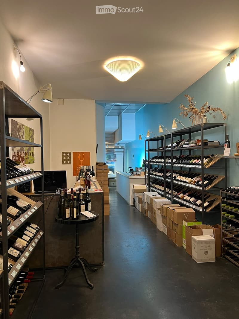 Wine shop interior with shelves filled with wine bottles, a round table with several bottles, and modern lighting.