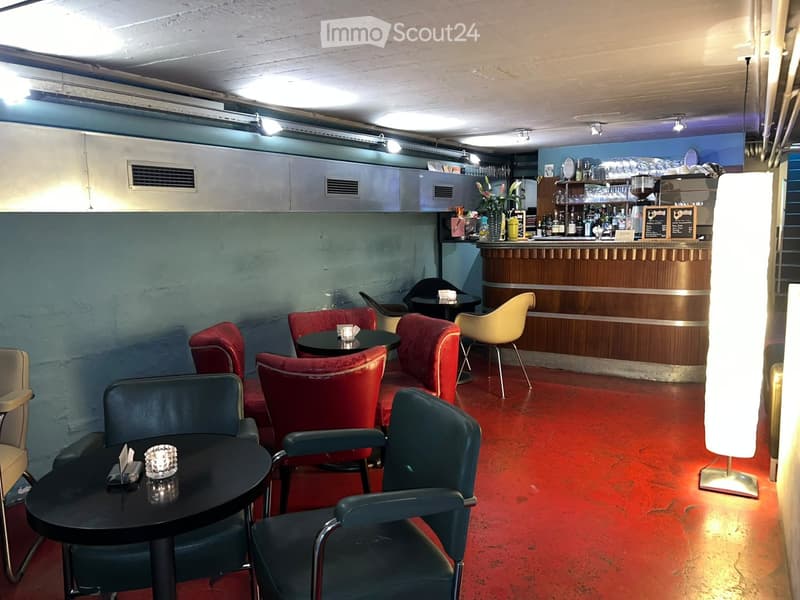 A stylish bar area with red carpeting, black tables, and colorful chairs, including red, yellow, and blue seating options.
