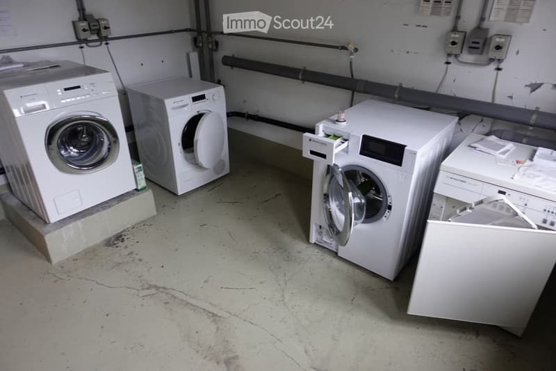 Utility room with white washing machine, dishwasher, and other appliances on a concrete floor.