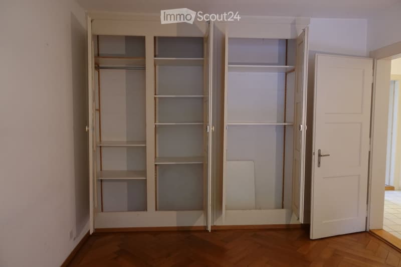 Empty room with wooden flooring, white walls, and built-in closet units with open shelves and doors.