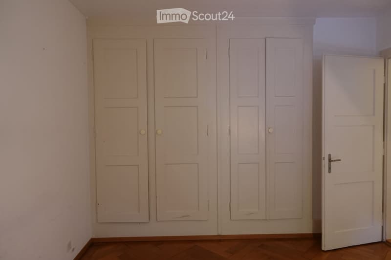 Empty room with wooden flooring and multiple white doors, including a double door and a single door.