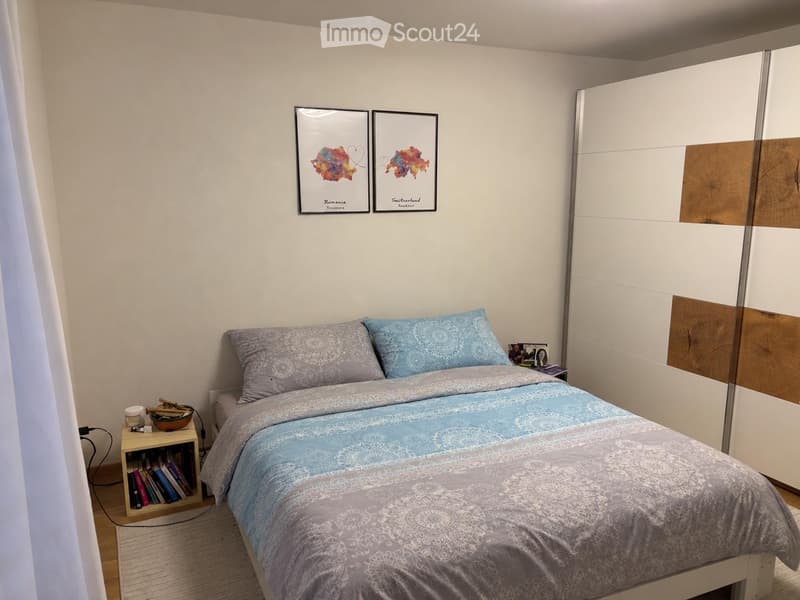 A modern bedroom with a double bed, nightstand, mirror wardrobe, and decorative picture frames on the wall.