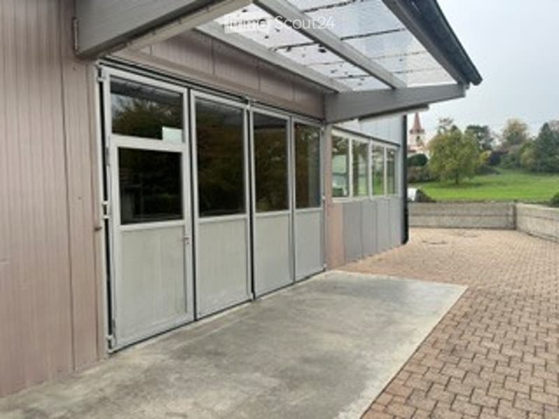Modern building exterior with large sliding glass doors, brick pavement, and a covered walkway.