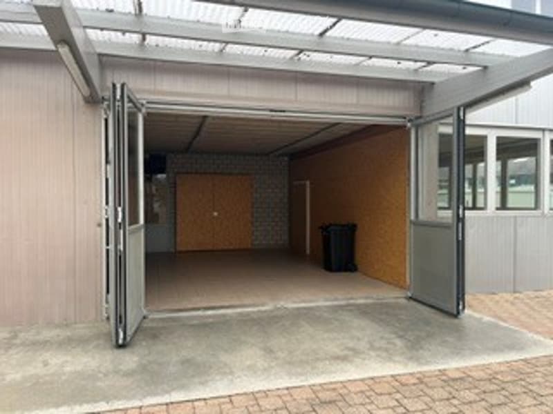 A modern garage with large, open doors, concrete floor, and a covered entrance area.