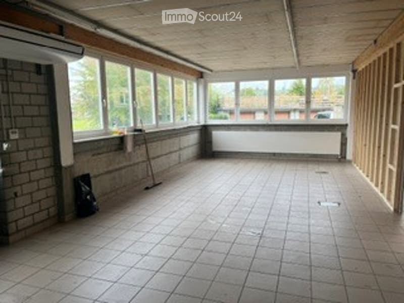 Empty room with tiled floor, large windows, exposed wooden beams, and a broom leaning against the wall.