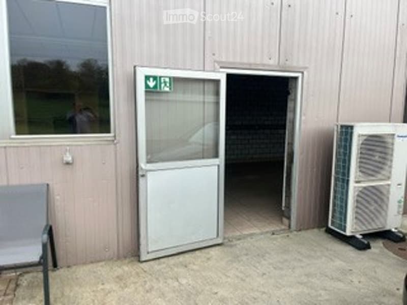 An exterior view of a building entrance with a glass door, a chair, and an air conditioning unit placed nearby.