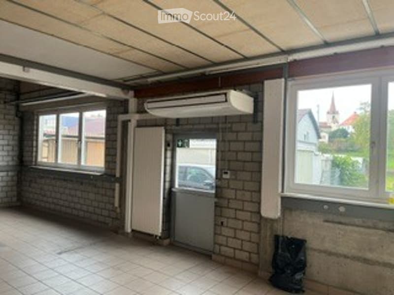Empty garage or storage space with brick walls, tiled floor, windows, and a door leading outside.