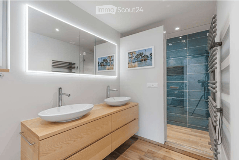 Modern bathroom with double sinks, sleek wooden vanity, large mirror with LED lighting, and a glass-enclosed shower area.