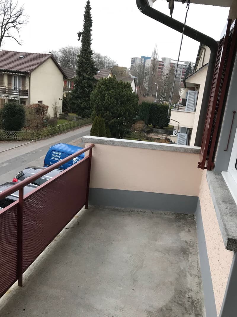 Balcony with metal railing, concrete floor, and view of street and neighboring houses.