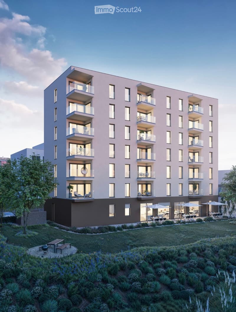 Modern multi-story residential building with balconies, surrounded by landscaped garden area with seating and outdoor furniture.
