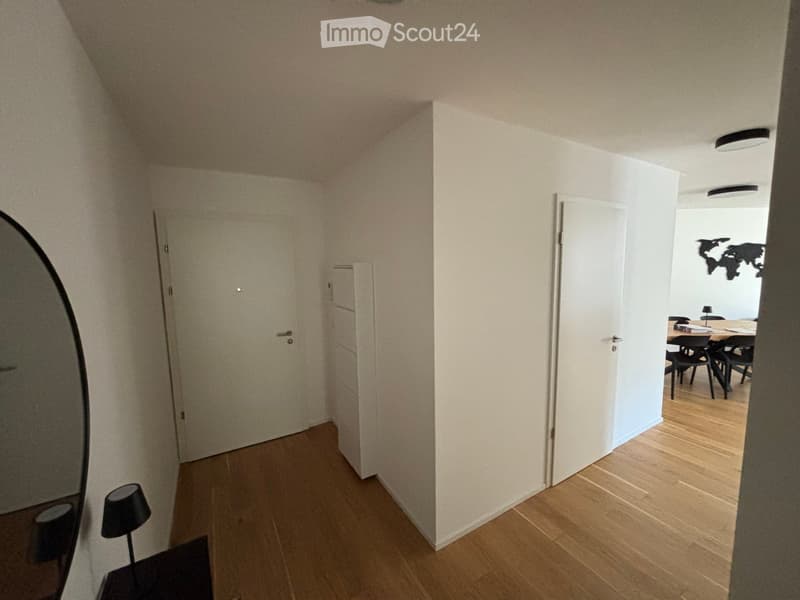 A narrow hallway with wooden flooring, white walls, and two doors leading to other rooms. A small lamp is visible on the left side.