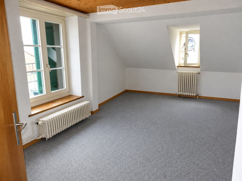 Empty room with grey carpet, white walls, wooden trim, radiators, and large windows with wooden sills.