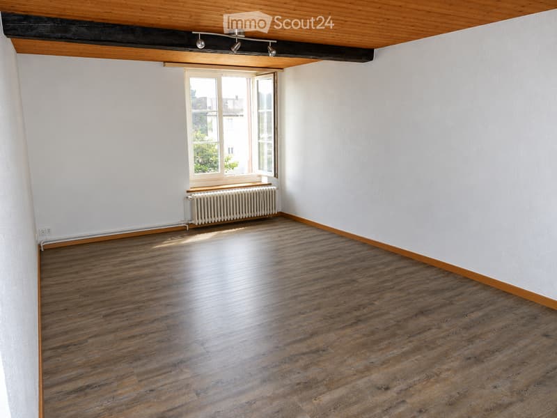 Empty room with wooden flooring, white walls, and a large window with a radiator below it.
