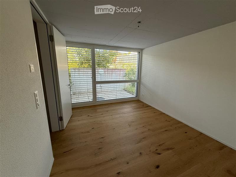 Empty room with wooden flooring, white walls, and large windows with blinds. No furniture or equipment present.