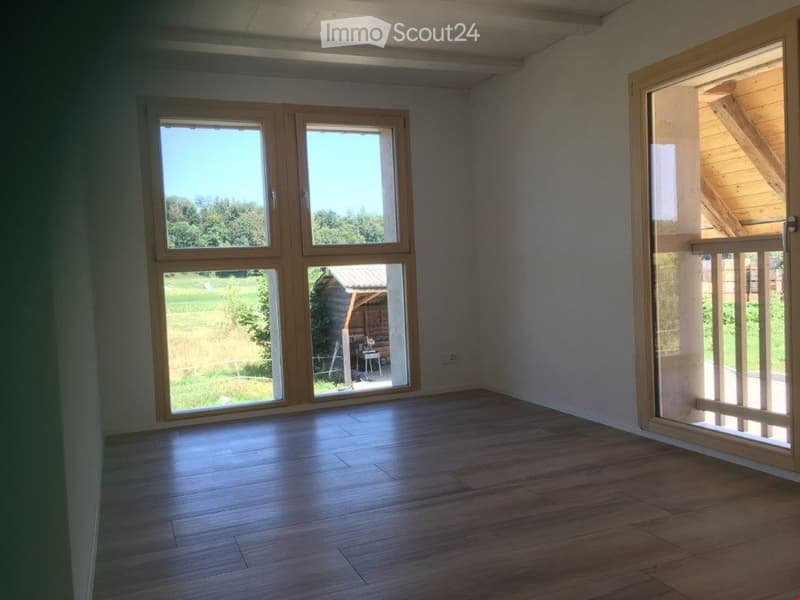 Empty room with wooden flooring, large windows, and a sliding glass door leading to an outdoor area.
