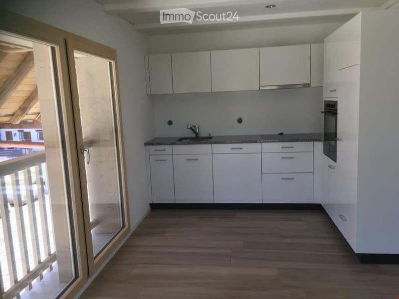 Modern, unfurnished kitchen with white cabinets, granite countertops, and a wooden floor. Features a large window with a view to a balcony.
