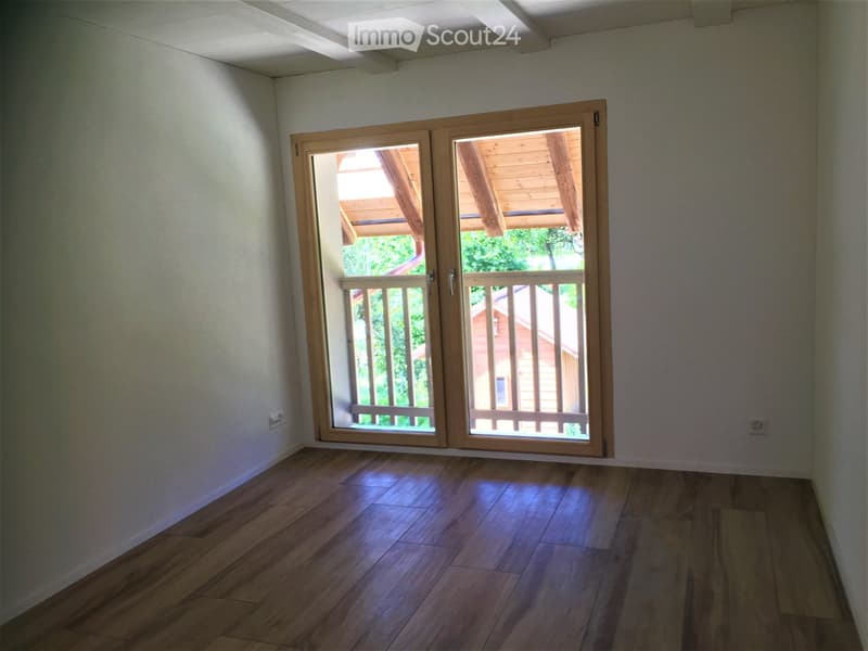 Empty room with wooden flooring and large sliding glass doors leading to a wooden deck outdoors.