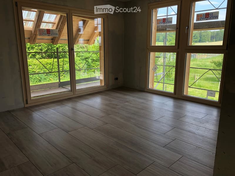 Empty room with wooden flooring and large windows offering a view of greenery outside. No furniture or equipment present.